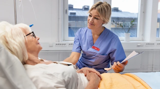 A nurse is sitting next to a bed where an elderly woman is lying.