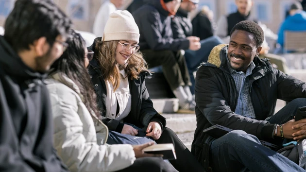 Several students in winter attire in the warming spring sun on Campus Umeå.