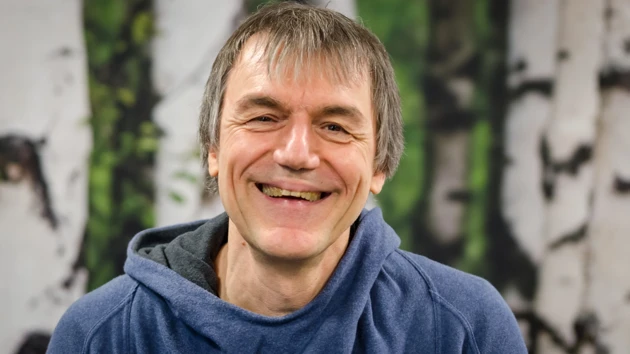 A man in a blue hoodie smiles at the camera