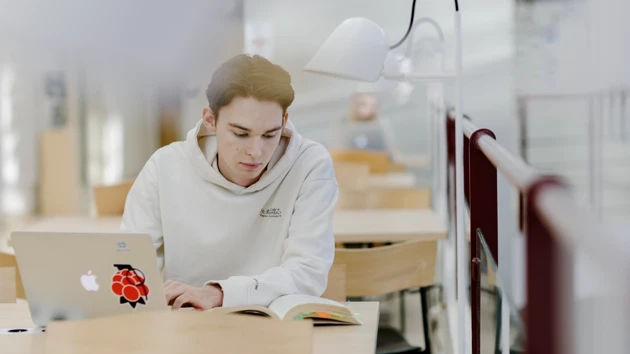 Studenten Hugo pluggar med dator och anteckningsblock.